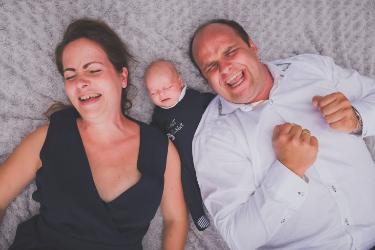 Eltern liegen lachend mit ihrem Baby auf einer Decke