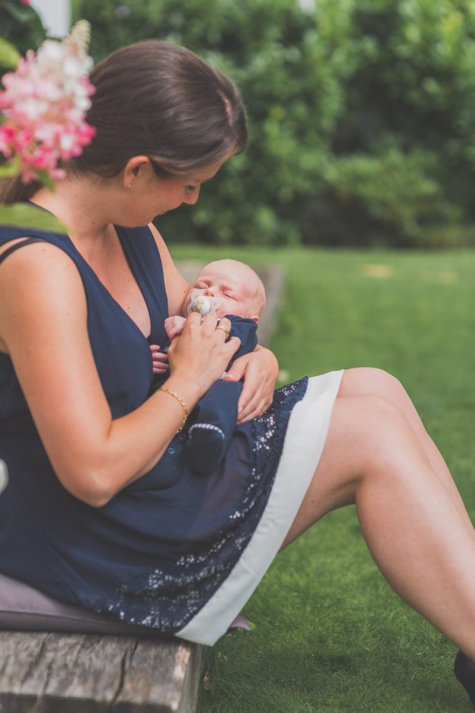 Mutter sitzt im Garten und blickt auf ihr Baby im Arm