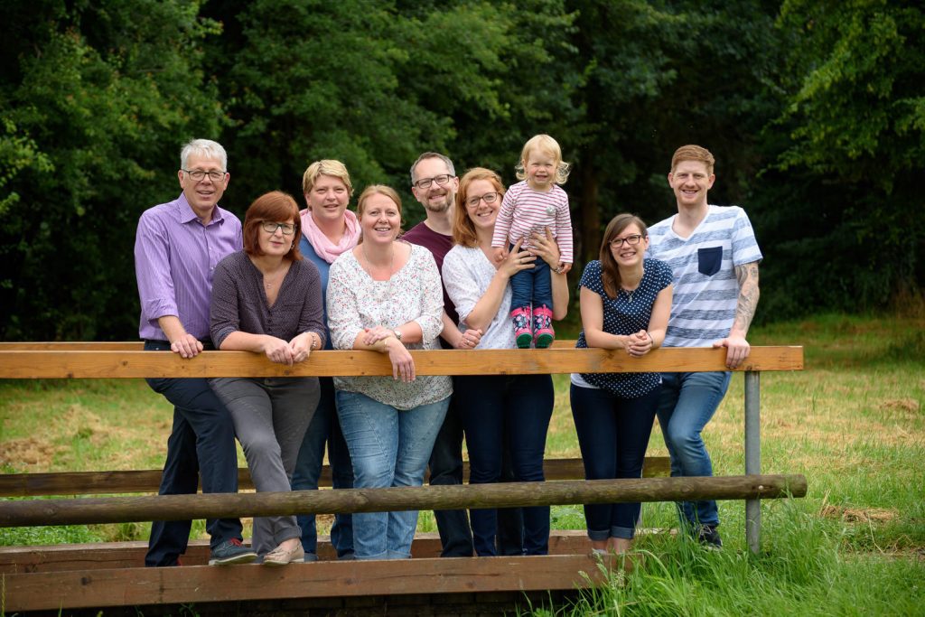 Großfamilie steht gemeinsam an einem Holzzaun im Grünen