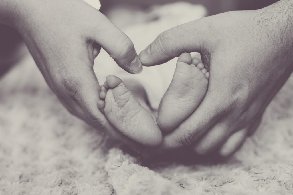 Elternhände formen ein Herz um kleine Babyfüße