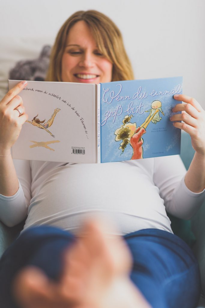 Schwangere Frau liest ein Kinderbuch, das auf ihrem Bauch liegt