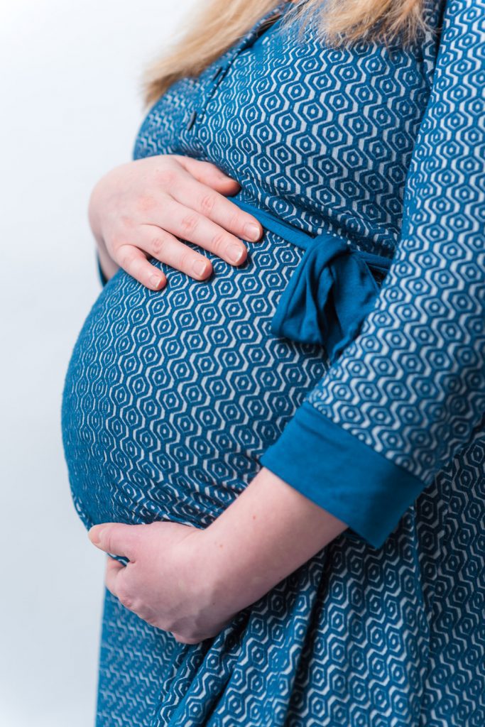 Schwangere Frau im blauen Kleid hält ihren Babybauch
