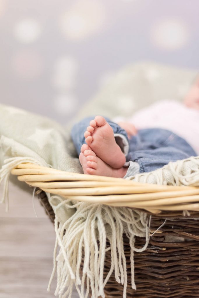 Babyfüße ragen aus einem Weidenkorb mit Decke