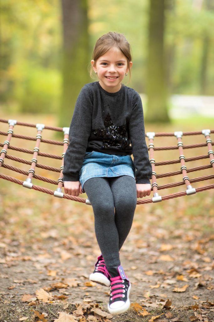 Mädchen sitzt auf einer Netzschaukel im Herbstwald