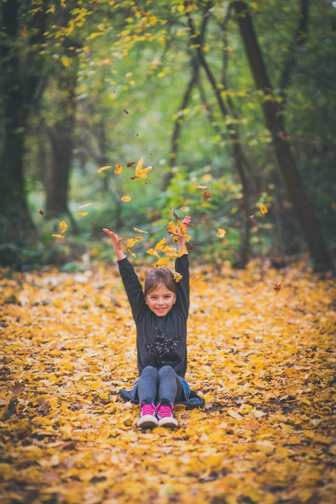 Kind wirft im Herbstwald Laub in die Luft