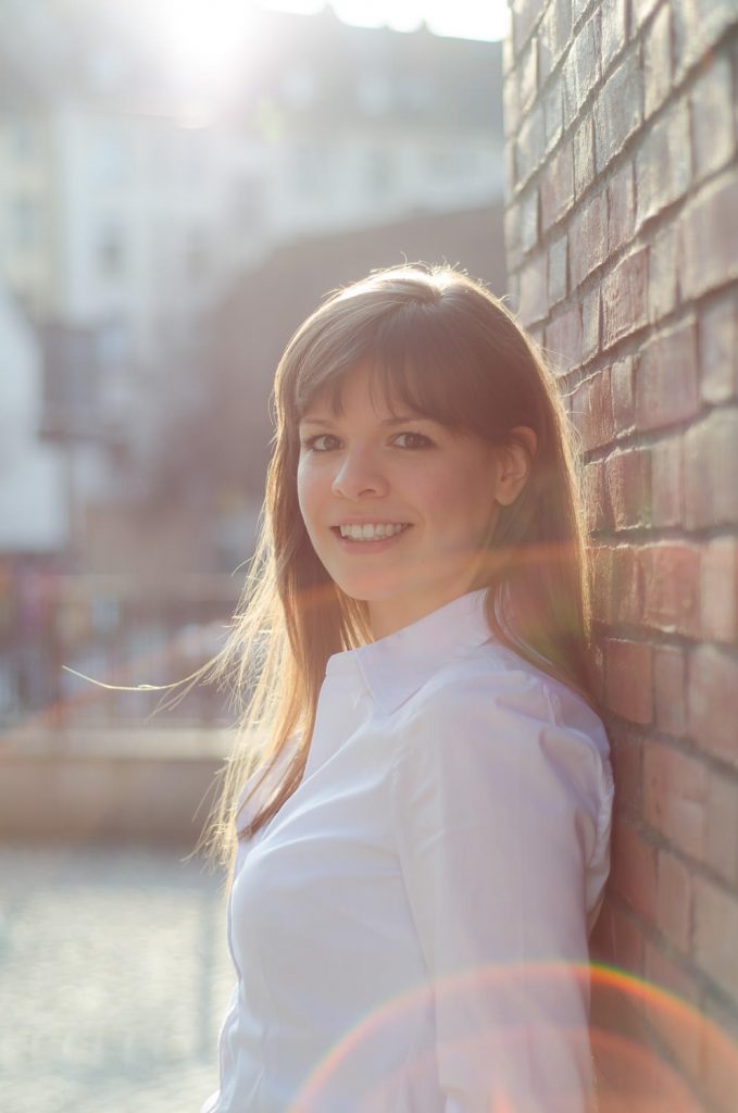 Porträt einer Frau mit langen Haaren im Gegenlicht an einer Backsteinwand