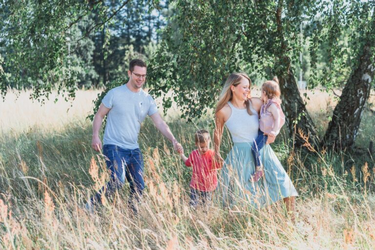 Familie mit zwei Kindern spaziert durch hohes Gras unter Birken