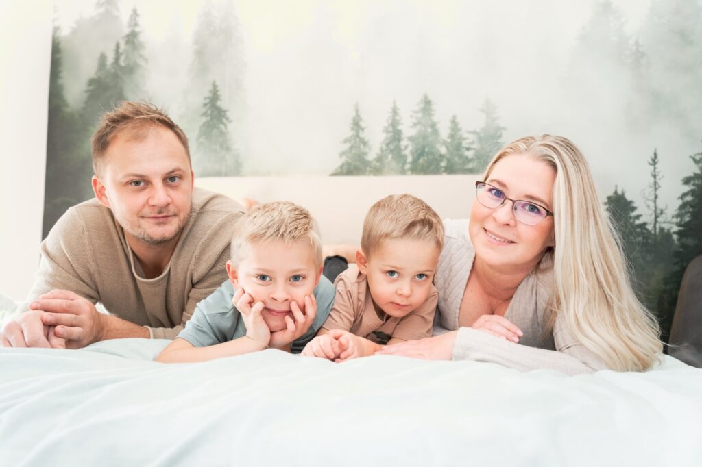 Familie mit zwei kleinen Söhnen liegt lachend auf dem Bett